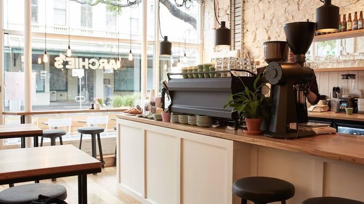 Café counter with an espresso machine and stacked cups, lit by daylight from the street windows